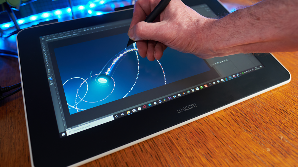 A person drawing on a Wacom One tablet on a wooden desk.