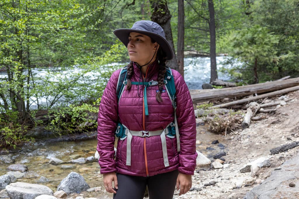 Woman hiking along a river in the forest wearing the Patagonia Quandary Brimmer sun hat and Nano Puff jacket