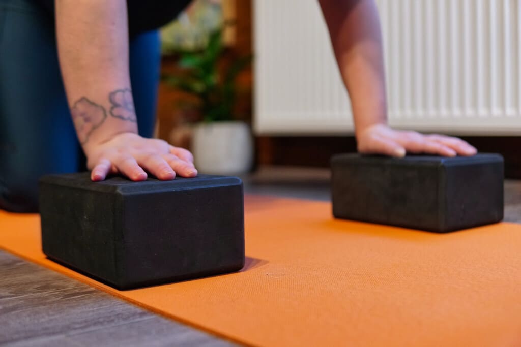 woman practicing yoga with black blocks on orange mat